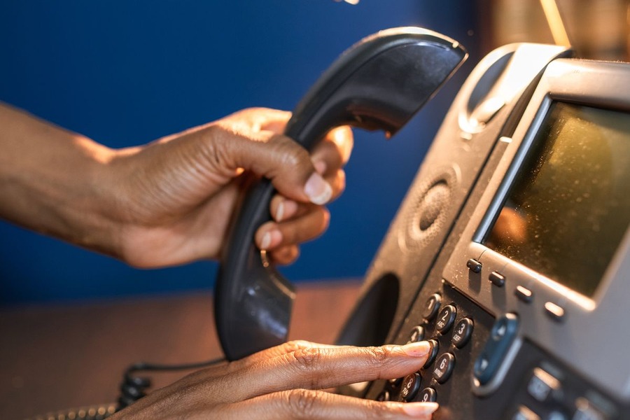 Personne composant un numéro sur un téléphone fixe de bureau