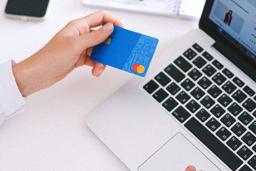 Personne tenant une carte bancaire devant un ordinateur portable ouvert