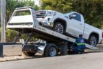 Un opérateur de dépanneuse charge un véhicule utilitaire blanc sur un camion de remorquage