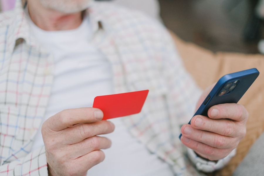 Mains d'une personne âgée tenant une carte bancaire et un smartphone
