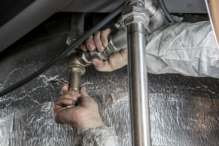 Une personne répare une canalisation sous un meuble, outils de plomberie à la main